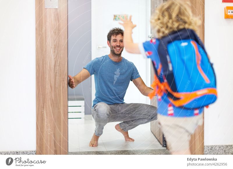 Little boy running towards his father waiting for him at home education school backpack leaving morning front door entrance hall real people affectionate