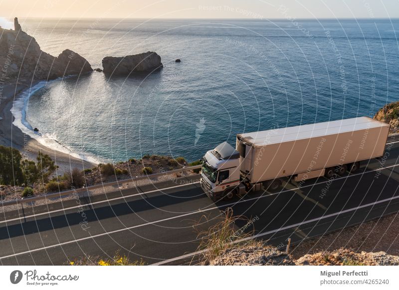 Truck with refrigerated semi-trailer driving along a road by the sea with a beach in the background. Refrigerated Beach truck transport Street Exterior shot