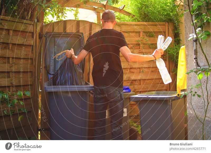 One person performing a selective sorting of household waste in recycling bins. Man putting plastic bottles in a yellow container and garbage in a bag in a green container.