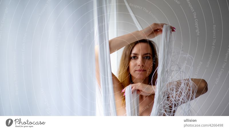 muscular beautiful young attractive sexy woman by the window, playing with the falling white threads of a curtain, copy space Woman girl string textile industry