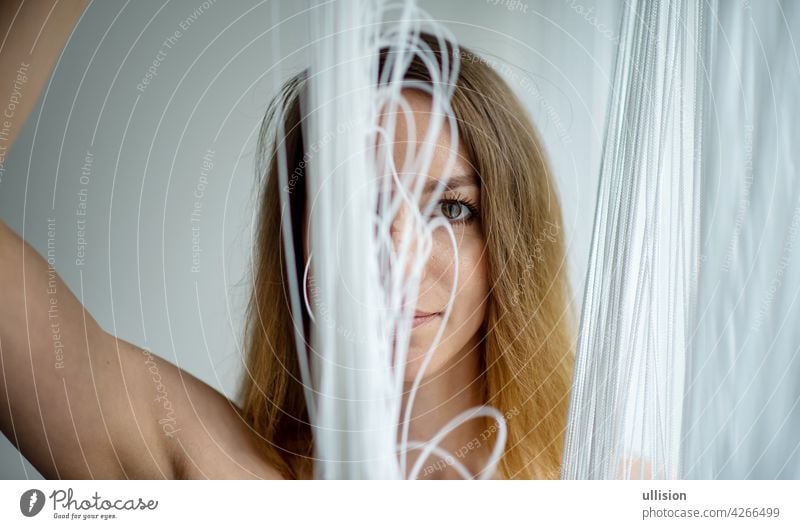 Portrait of a beautiful young attractive sexy woman by the window, playing with the falling white threads of a curtain of threads, copy space Woman girl string