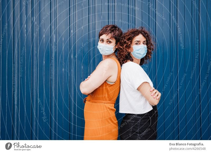 two caucasian women outdoors wearing face mask keeping social distance in Pandemic during corona virus elbow covid avoid prevention people generation safety
