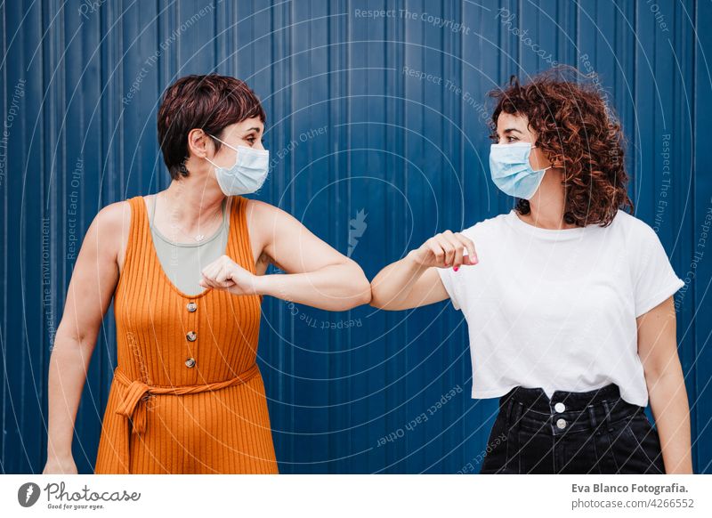 two caucasian women outdoors wearing face mask keeping social distance in Pandemic during corona virus elbow covid avoid prevention people generation safety