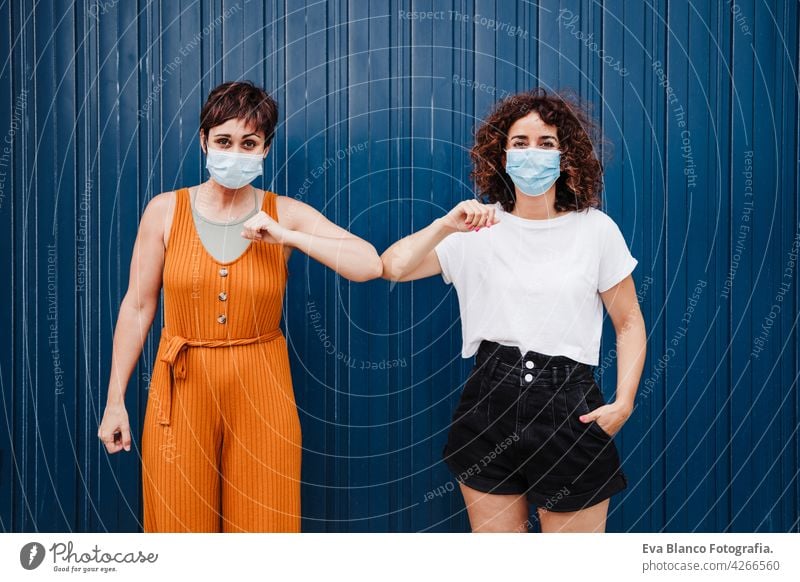 two caucasian women outdoors wearing face mask greeting with elbows. Pandemic during corona virus social distance concept. covid avoid prevention people