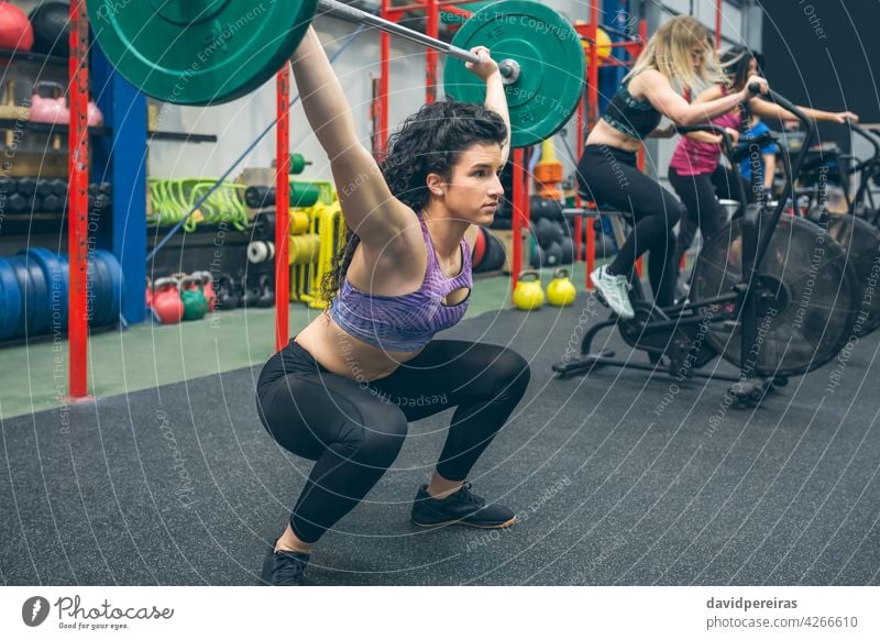 Woman practicing weightlifting in the gym woman dumbbell snatch arms up determination overcoming over head squat sportswoman self confident train strength