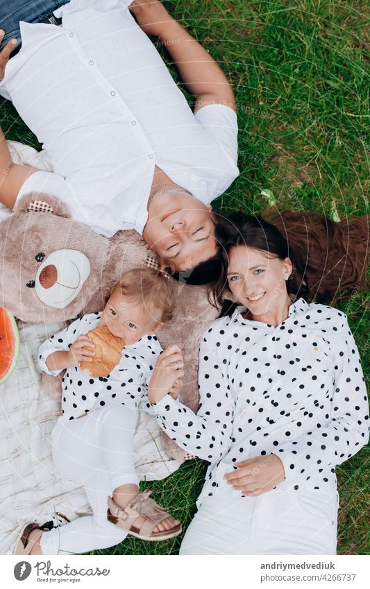 Mom, dad and daughter lying on the picnic with teddy bear. The concept of summer holiday. Mother's, father's, baby's day. Family spending time together on nature. Family look
