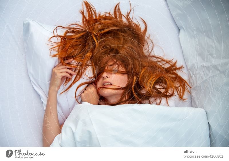 Attractive, young, sexy, red-haired woman, Redhead, hair wild on the sheets, mouth open, lying in fresh white sheets in bedroom, Hotel bed, copy space. red hair