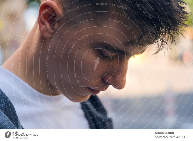 closeup of a pensive teenager looking down portrait young man sensitive tranquil shadow sun backlit sunlight handsome beautiful outdoor street bokeh male casual