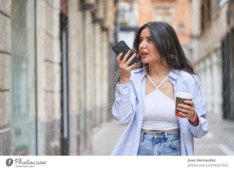 young woman sending an audio message with smart phone arabic muslim lady mobile phone arabian cellphone ethnic expression expressive coffee cardboard cup saudi