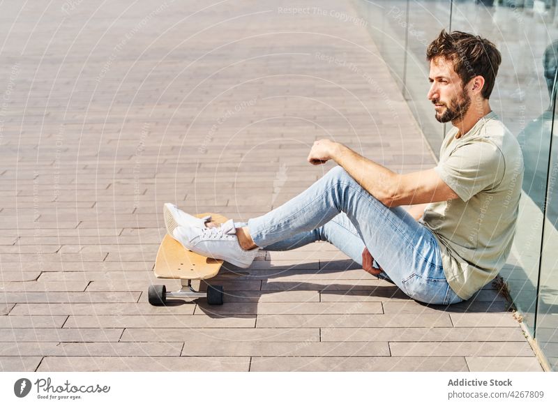 Serious man leaning on transparent barrier on embankment skateboard masculine chill relax cool river boardwalk recreation male waterfront sit casual quay fence