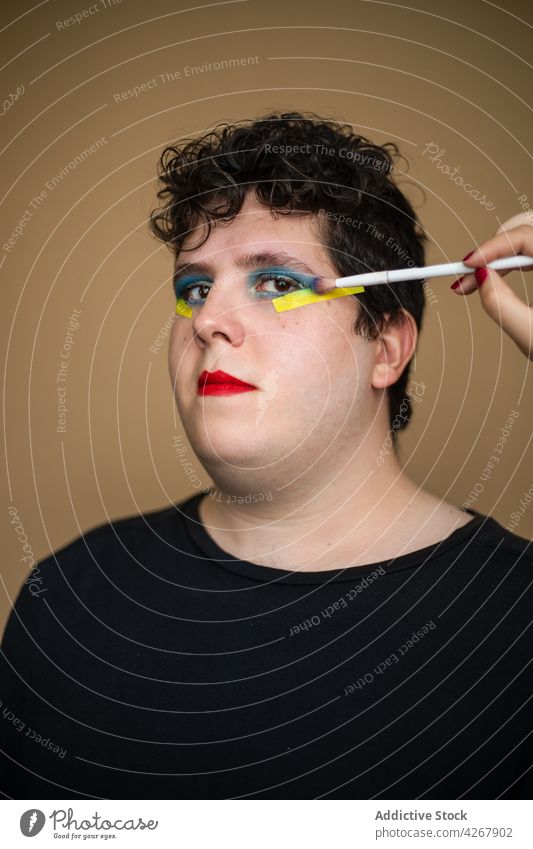 Visagiste applying bright eyeshadow on face of androgynous man visagiste brush makeup visage beauty queer male stylist alternative unusual gender cosmetic