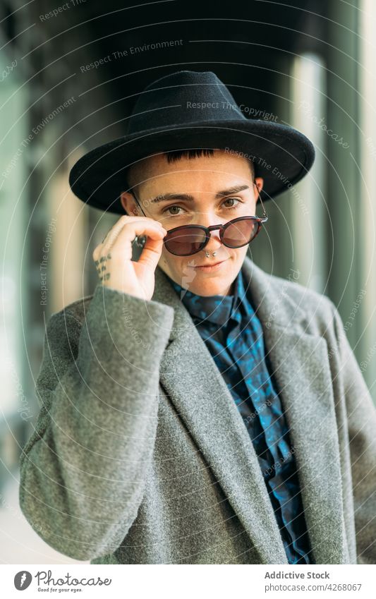 Queer in stylish outerwear and sunglasses outdoors transgender person style fashion individuality accept identity tattoo portrait queer androgynous sincere