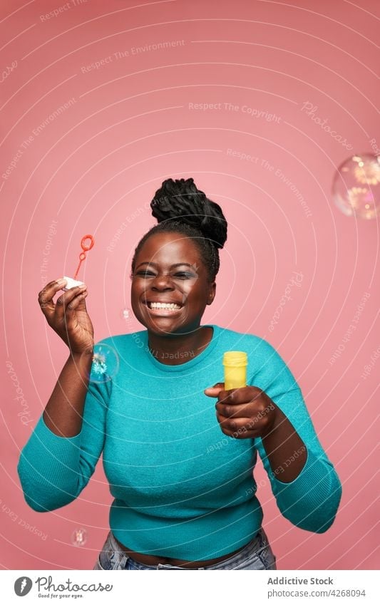 Joyful black woman blowing soap bubbles in studio ethnic joyful african american happy colorful vivid playful toy having fun smile entertain positive cheerful