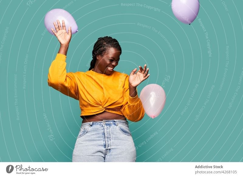 Joyful black woman playing with balloons in studio excited happy joyful playful laugh eyes closed vivid having fun style colorful cheerful bright stand outfit