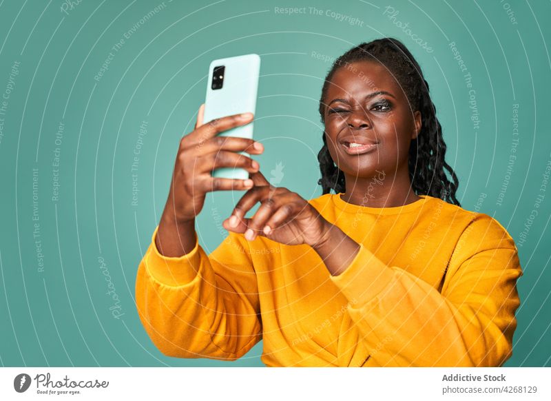 Content black woman winking and taking selfie on smartphone take photo happy cheerful photography grimace vivid social media self portrait device optimist