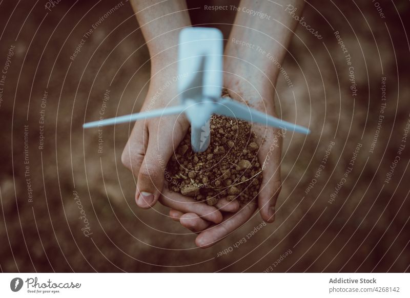 Person with handful of soil and mill miniature person windmill ecology alternative energy concept renewal power industry turbine plantation tool ground