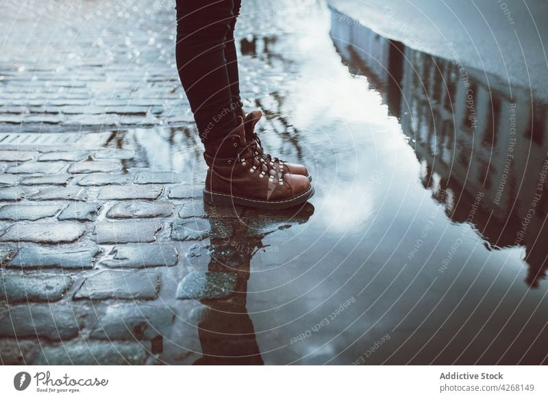 Crop person in boots on wet pavement puddle building reflection architecture facade mirror urban style tile shiny house exterior stand alone magnificent old