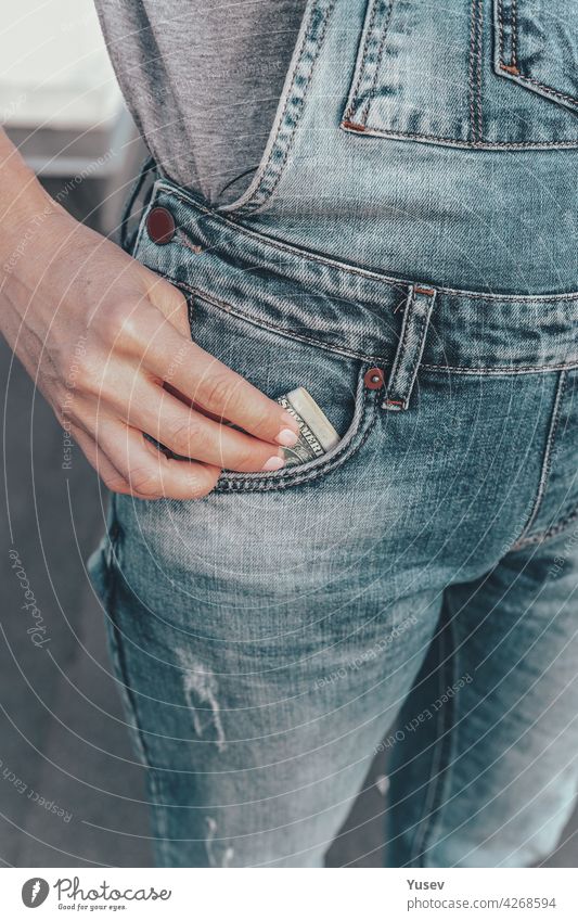A womans hand takes out US dollar bills from her jeans pocket. The concept of finance, savings, financial expenses. Close-up. Vertical shot taking blue money