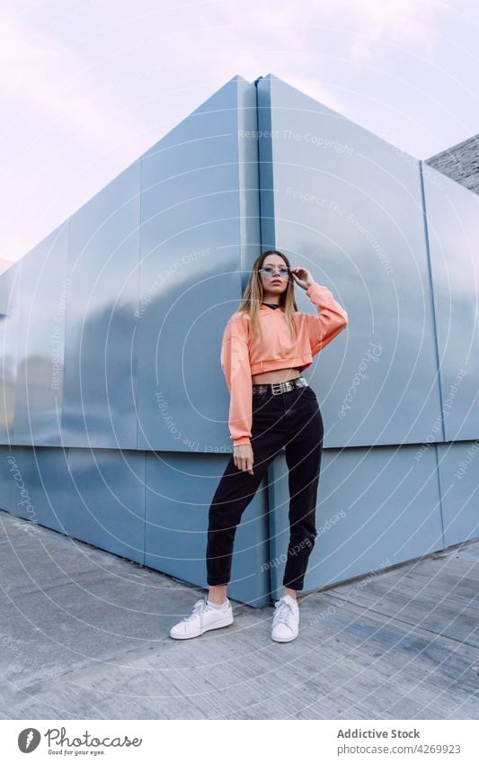 Stylish woman in sunglasses leaning on building wall style cool confident appearance charismatic provocative posture millennial youngster female jeans