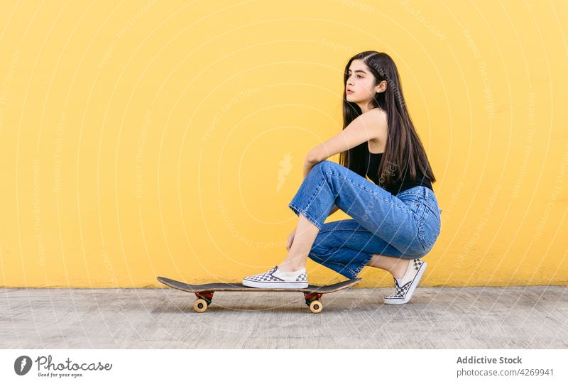 Skater squatting on skateboard on yellow background skateboarder sport dreamy casual style millennial charming walkway teenage skater outfit wistful pavement