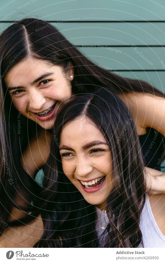 Smiling sisters with long hair on green background smile sincere friendly pleasant charming feminine lean on hand kind portrait teenage gaze candid content