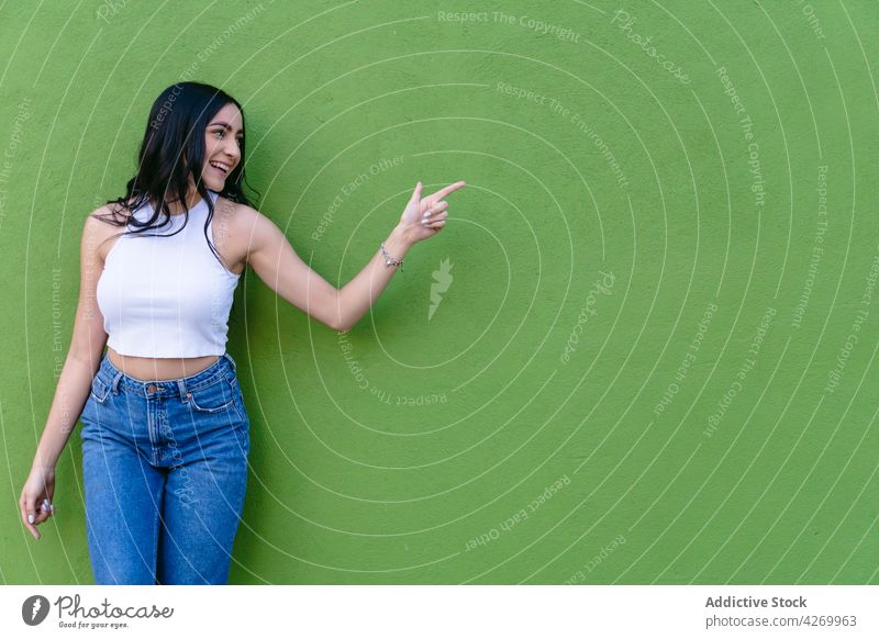 Cheerful teen pointing with finger on green background teenage cheerful feminine friendly pleasant charming casual style candid enjoy show indicate content