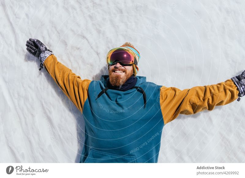 Smiling sportsman in goggles resting on snow in winter smile hipster outstretch freedom brutal glad cheerful athlete glove sincere macho masculine beard