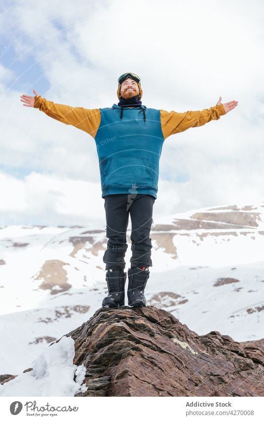 Smiling sportsman with outstretched arms on ridge in winter mountain freedom content life candid nature highland wintertime athlete cheerful masculine friendly