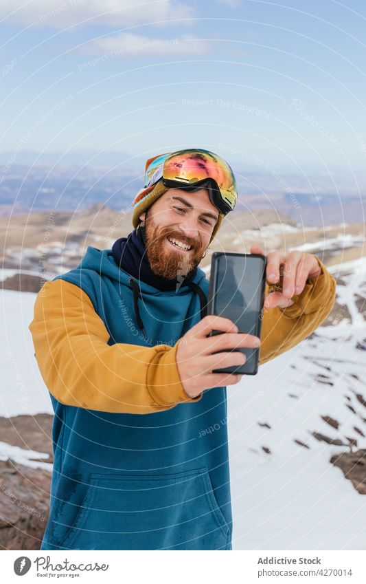 Smiling athlete taking selfie on smartphone in winter mountains sportsman cheerful memory moment snow hipster using gadget device goggles cellphone