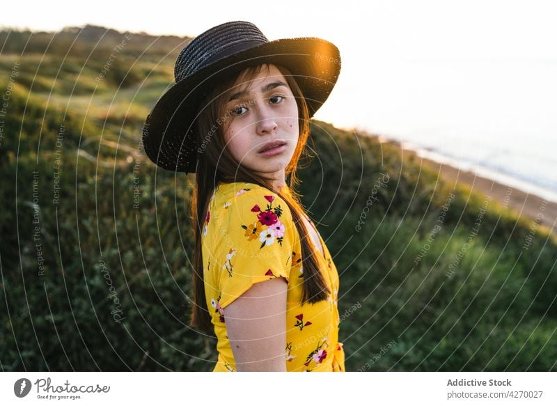 Young woman standing on grass lawn sundress countryside nature dreamy grassland meadow grassy young field hat appearance serene grace feminine carefree peaceful