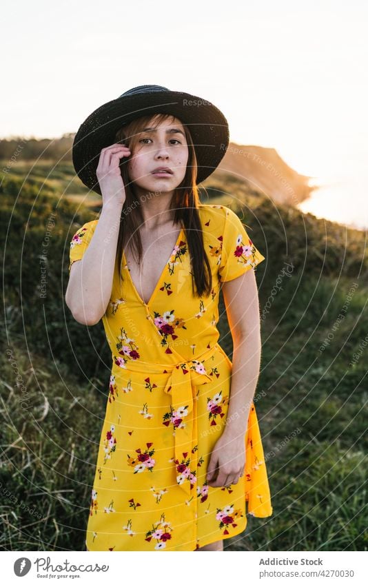 Young woman standing on grass lawn sundress countryside nature dreamy grassland meadow grassy young field hat appearance serene grace feminine carefree peaceful