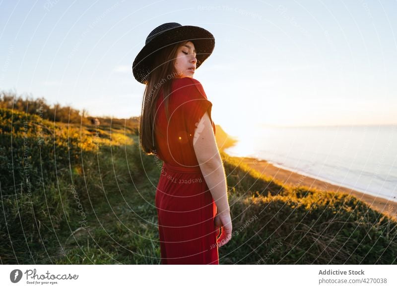 Young woman standing on grass lawn sundress countryside nature dreamy red grassland meadow grassy young field hat appearance serene grace feminine carefree
