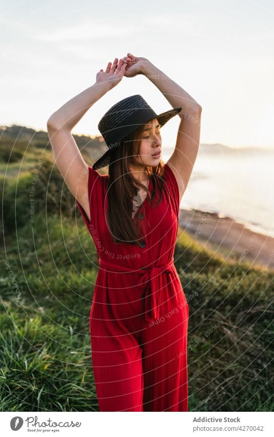 Young woman standing on grass lawn sundress countryside nature dreamy red grassland meadow grassy young field hat appearance serene grace feminine carefree