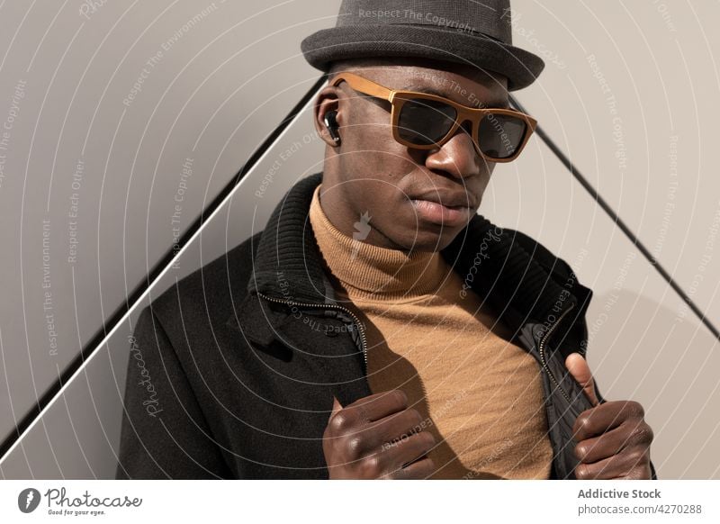 Stylish black man standing against white wall style outfit confident appearance trendy cool well dressed hat sunglasses individuality personality modern garment