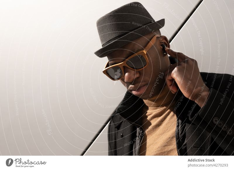 Stylish black man standing against white wall style outfit confident appearance trendy cool well dressed hat sunglasses individuality personality modern garment