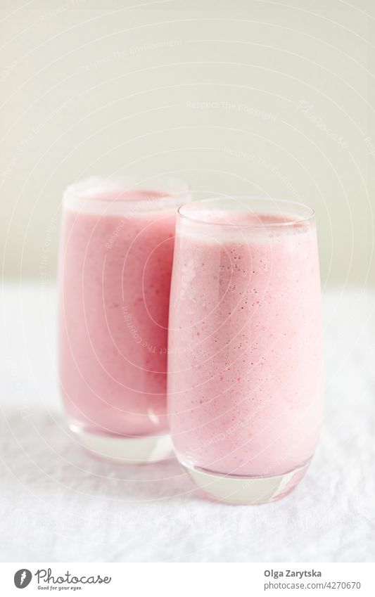 Two glasses of strawberry milkshake. smoothie pink red mint cold summer table white close up selective focus drink detox mixed blended two garnish pastel fruit