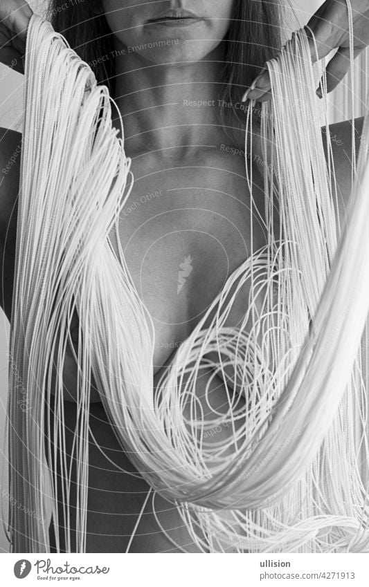 Attractive sexy body, chin and mouth of a young gorgeous woman, partially obscured by the white threads of a falling string curtain decorative in elegant shapes.