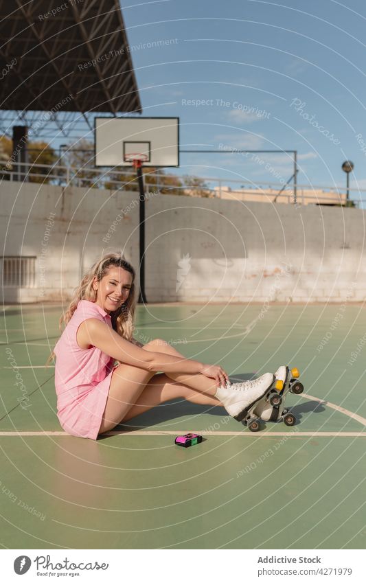 Happy woman in roller skates sitting on sports ground toothy smile skater cheerful activity happy hobby sporty energy content lifestyle trendy young sundress