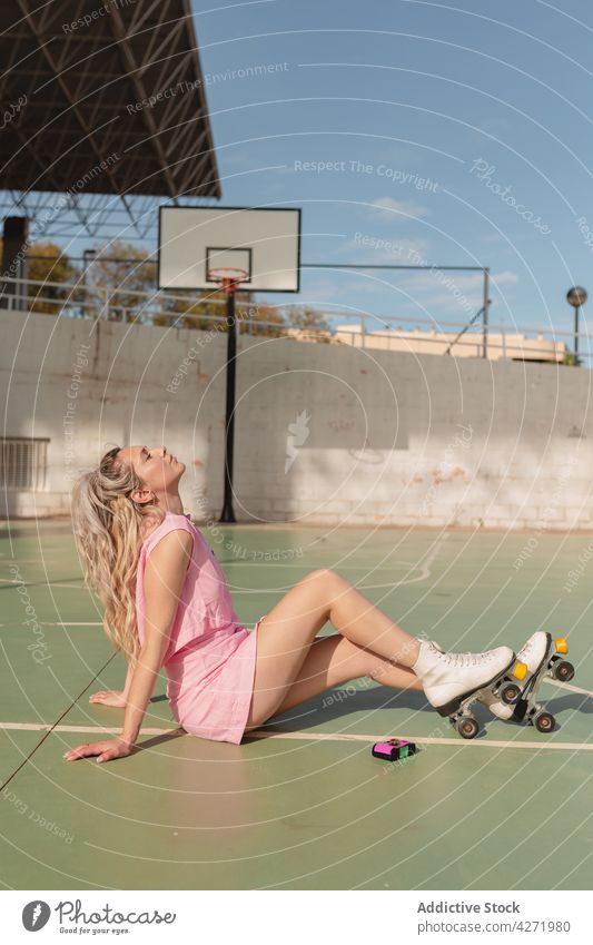 Woman in roller skates sitting on sports ground woman skater activity happy hobby enjoy eyes closed sporty energy lifestyle trendy young sundress positive fit
