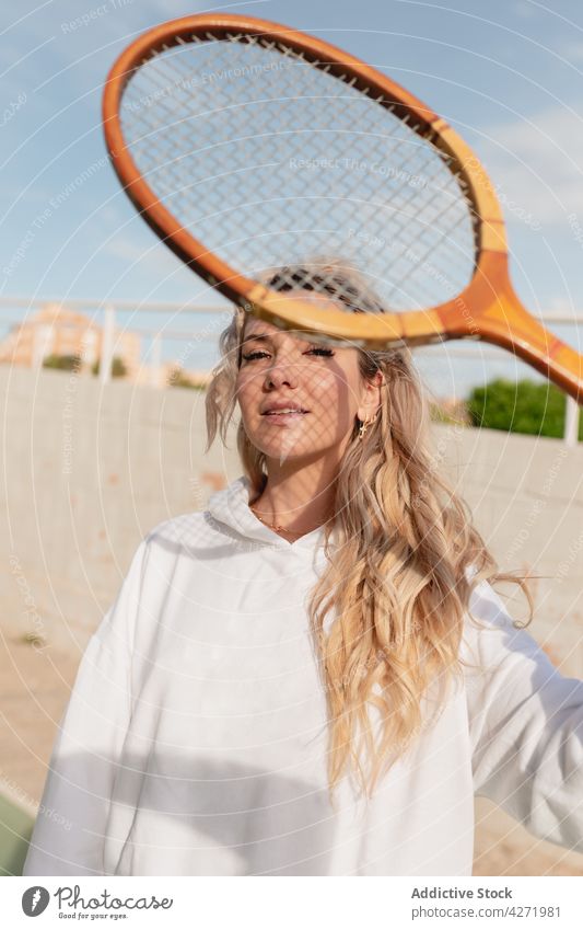 Attractive woman looking at camera through tennis racket on street positive glad sporty equipment young content lifestyle carefree pleasant attractive optimist