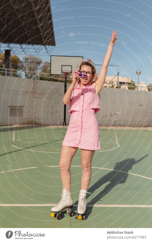 Cheerful woman on roller skates taking photo on instant camera skater take photo cheerful arm raised photography sports ground activity hobby style memory joy