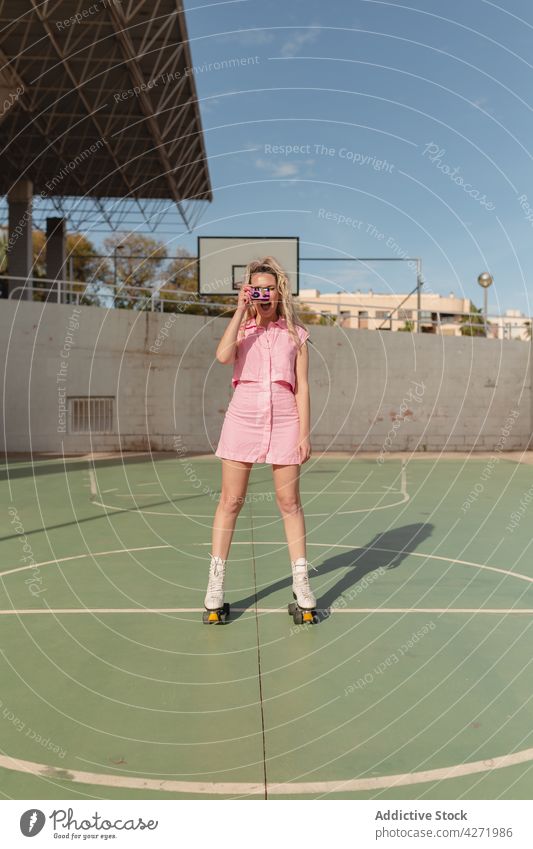 Cheerful woman on roller skates taking photo on instant camera skater take photo cheerful photography sports ground activity hobby style memory joy carefree