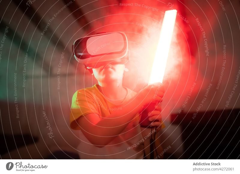 Cute child in VR goggles playing with toy sword virtual reality entertain innovation vr boy digital equipment fun kid casual neon illuminate darkness headset