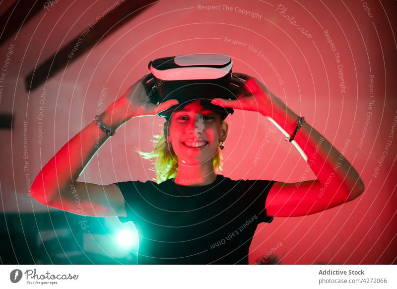 Smiling female in VR glasses in neon room woman vr modern headset studio virtual reality red light goggles device gadget experience contemporary equipment dark