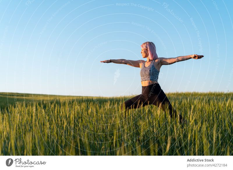 Woman standing in Warrior pose in countryside field woman warrior pose yoga healthy lifestyle wellbeing vitality energy outstretch practice wellness meadow