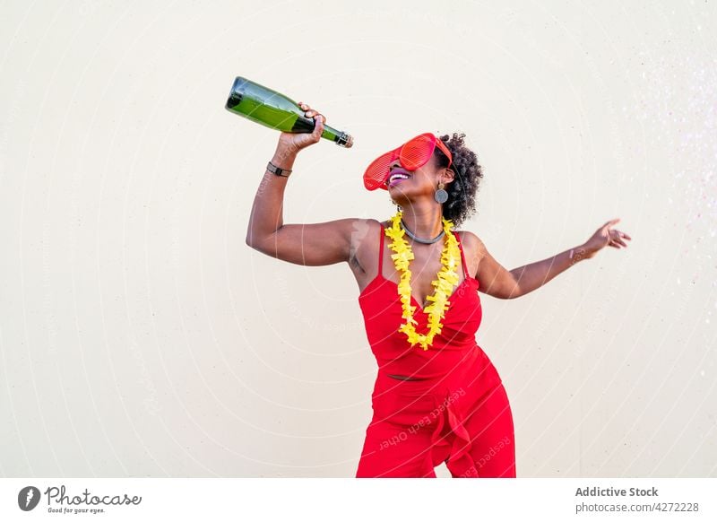 Happy black woman in stylish wear with bottle of champagne celebrate party style fashion happy drink alcohol glasses red apparel earring accessory trendy