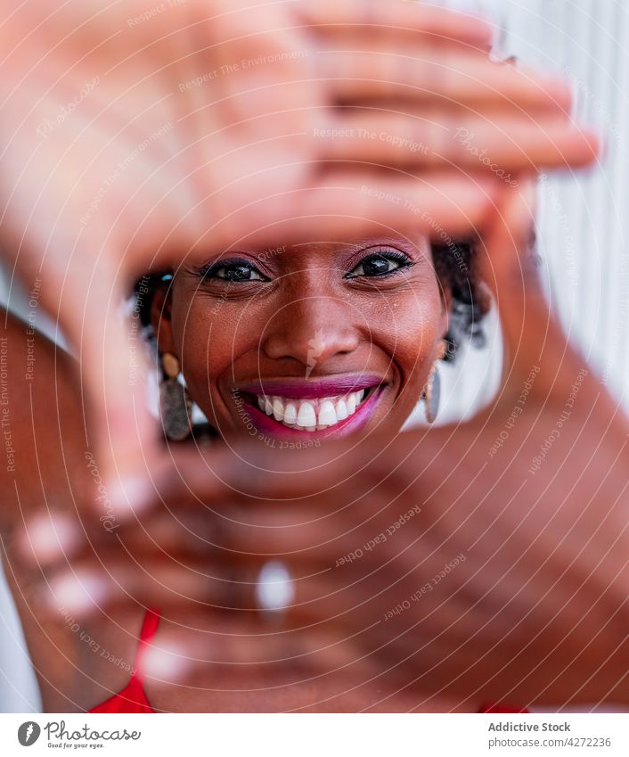 Black woman showing frame gesture in daylight photo perspective feminine sincere gaze gentle portrait style friendly red color photography intent tender