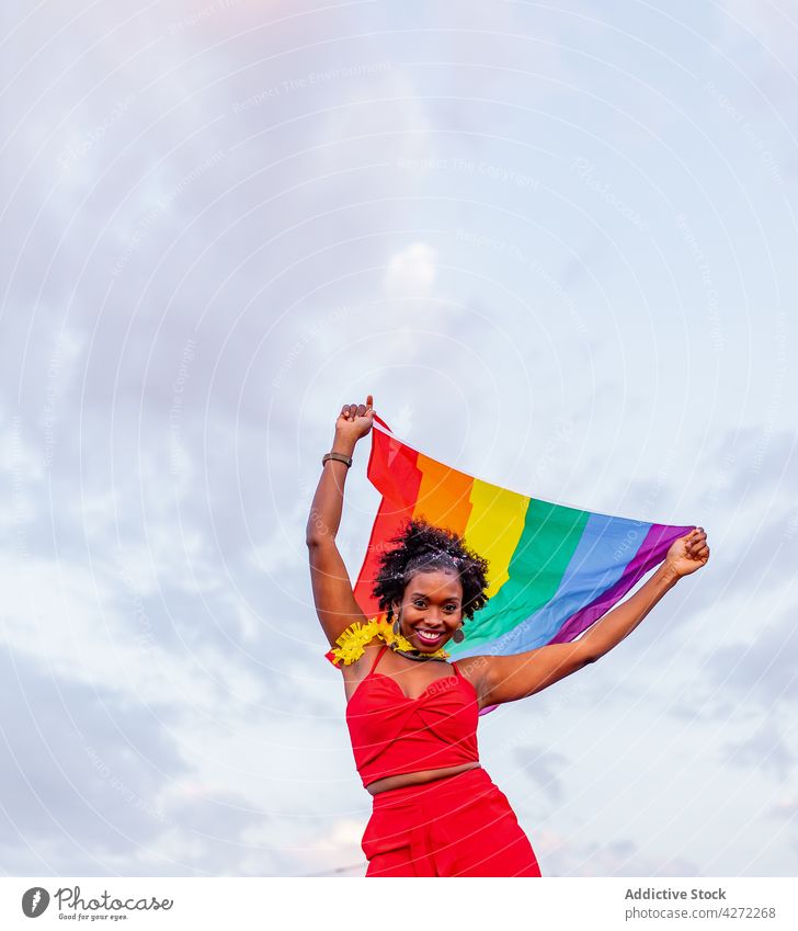 Smiling black woman with LGBTQ flag on road stylish fashion celebrate individuality pride spectrum raise arms raised lgbtq style equality tolerance rainbow