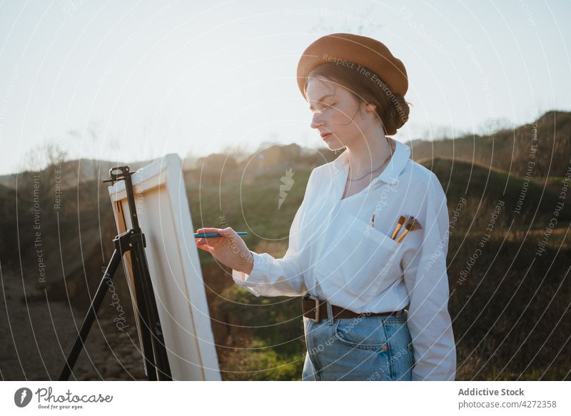 Female artist on shore near sand and sea while painting woman draw hobby canvas female young easel beret creative artwork style white shirt jeans talent lady