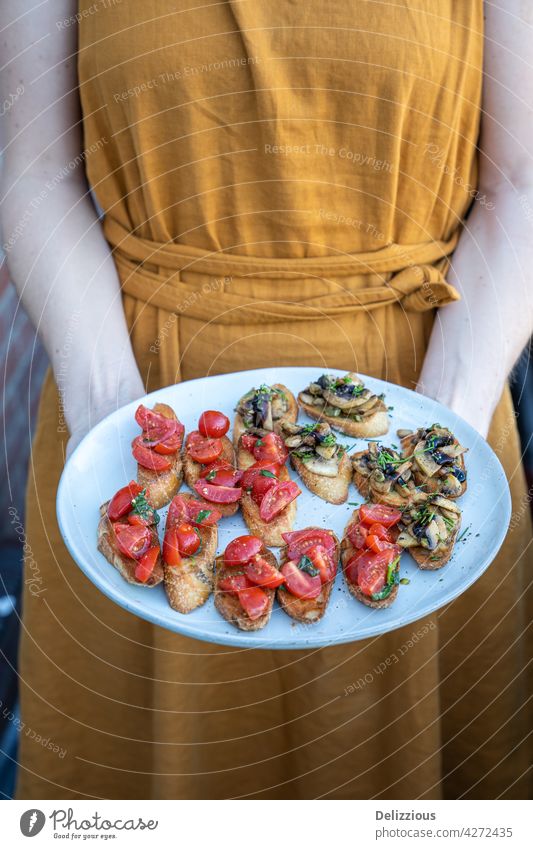 A woman in an orange dress holding a plate of home-made bruschetta with tomato and mushrooms, summer food bruchetta snack italian bread toast crostini